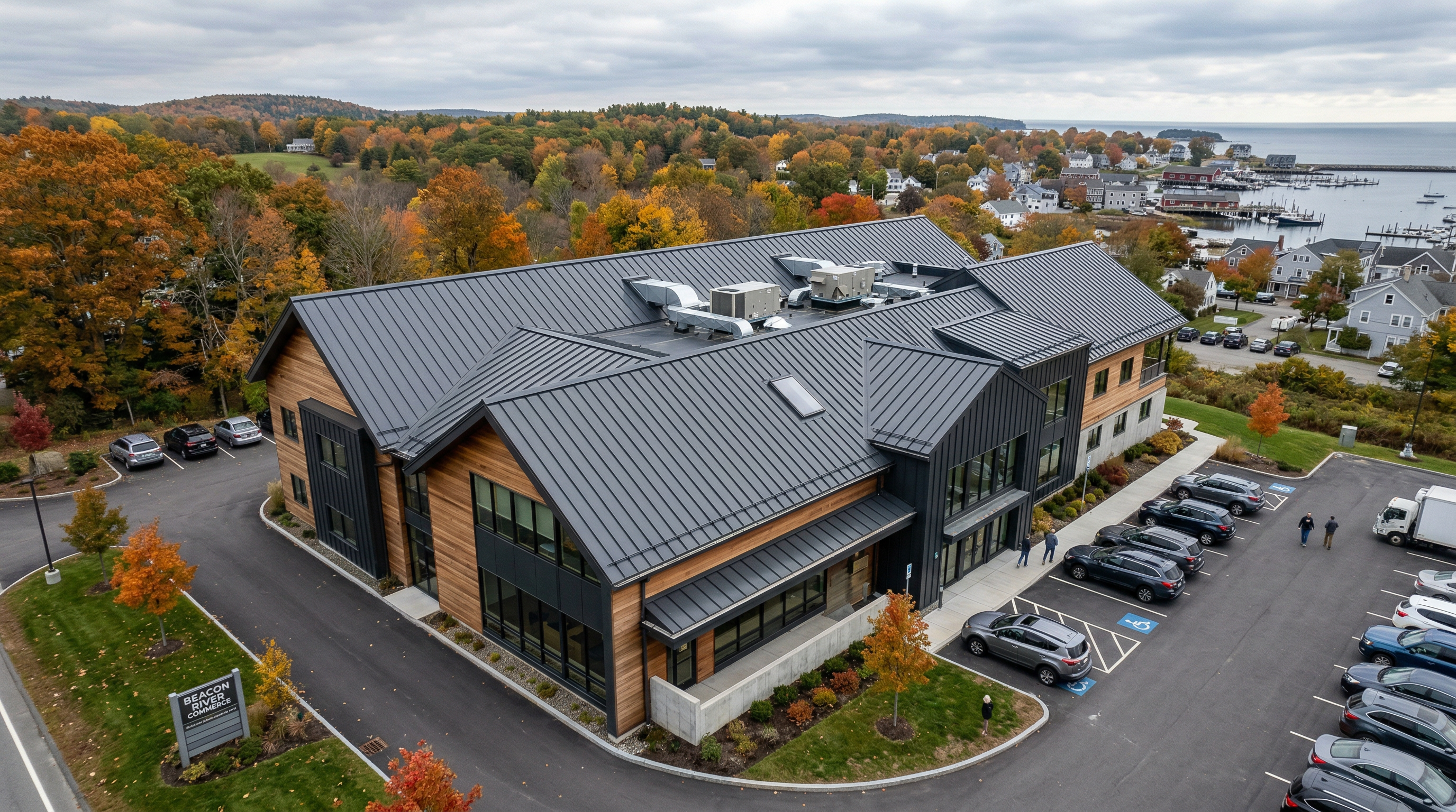 Modern commercial building with dark standing seam metal roof, aerial view showing New England coastal town